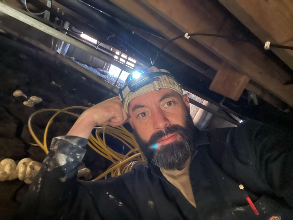 Michael Mentzer-Hernández wearing a headlamp while wiring under an Austin house